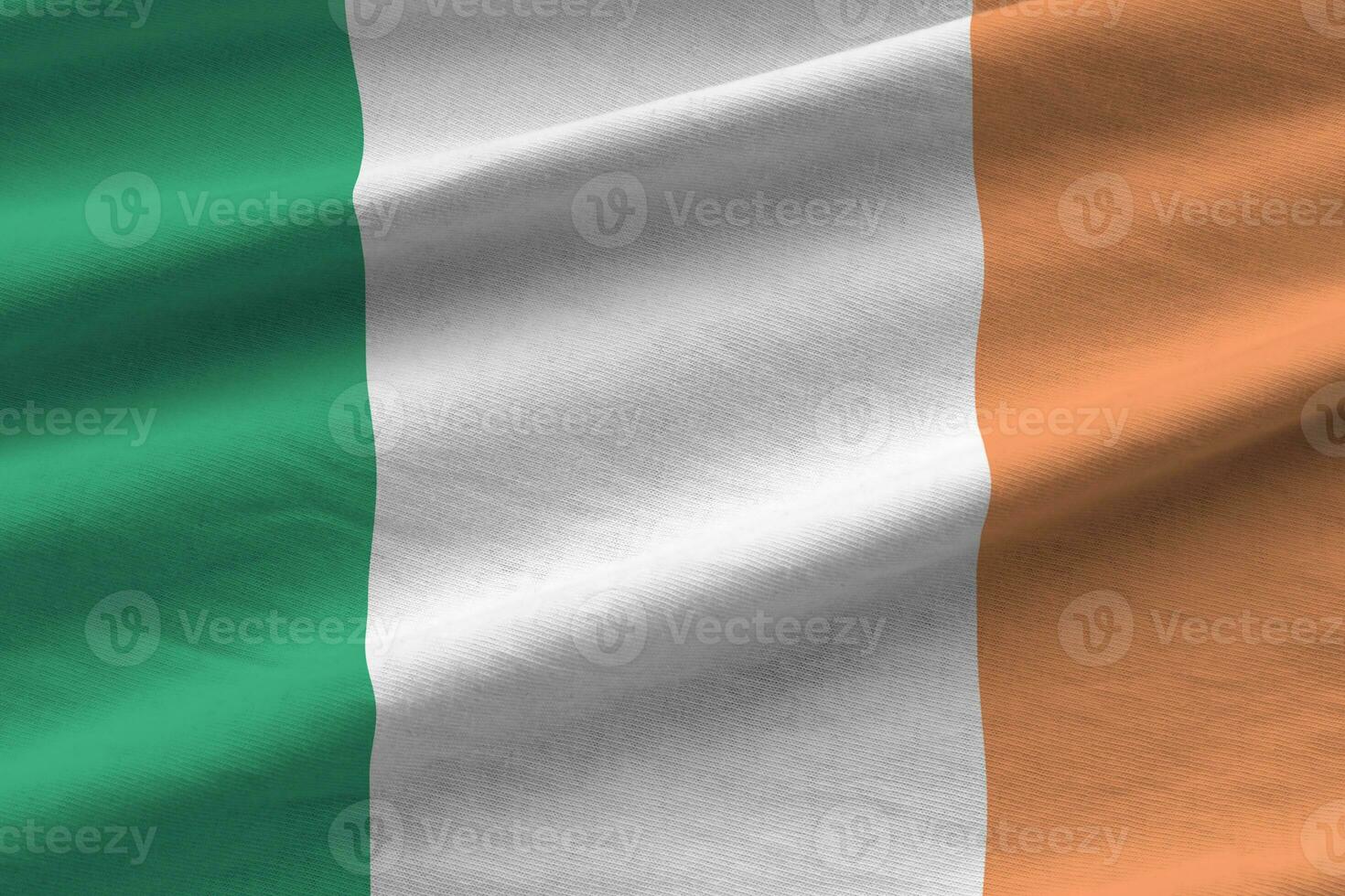 Ireland flag with big folds waving close up under the studio light indoors. The official symbols and colors in banner photo