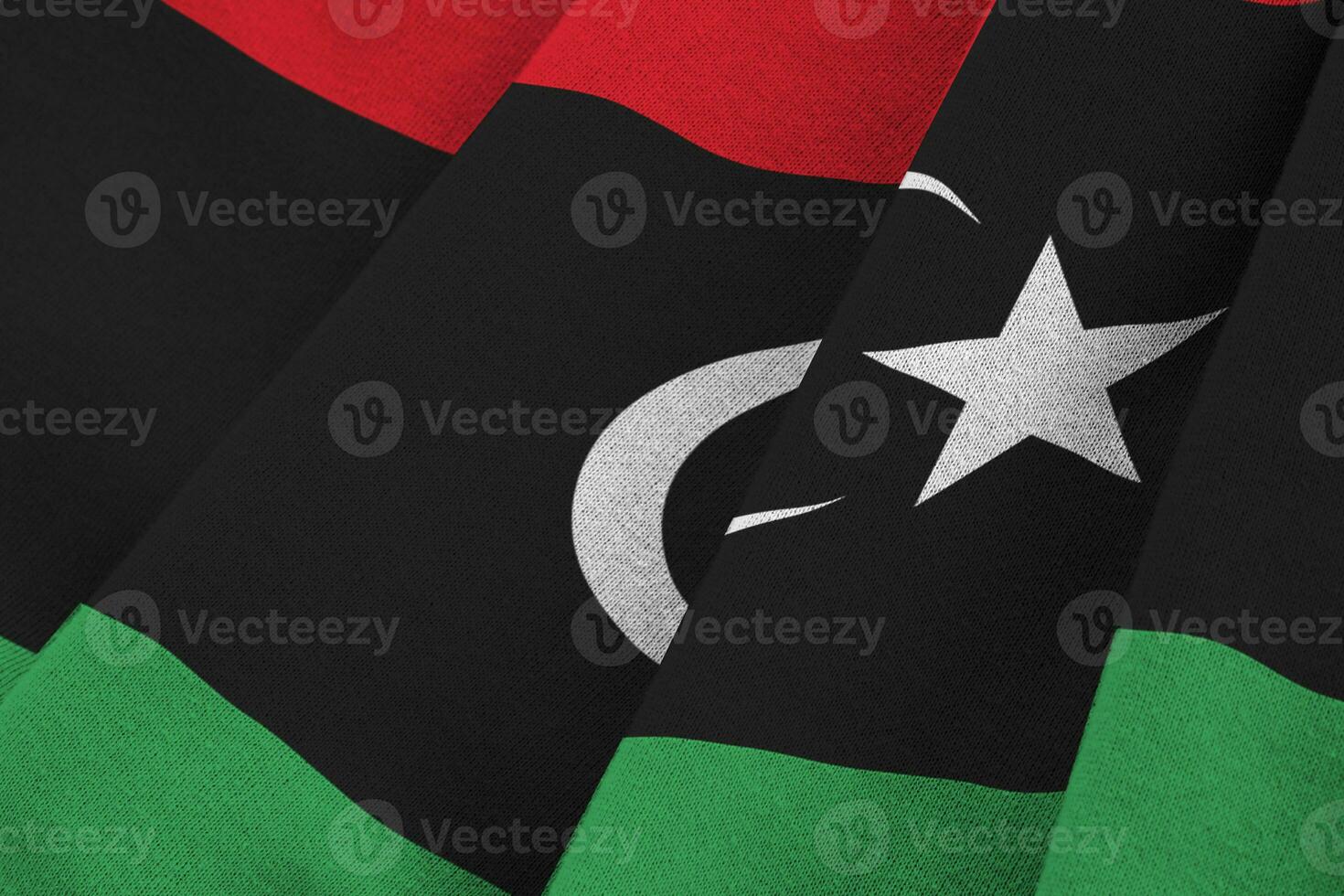 Libya flag with big folds waving close up under the studio light indoors. The official symbols and colors in banner photo