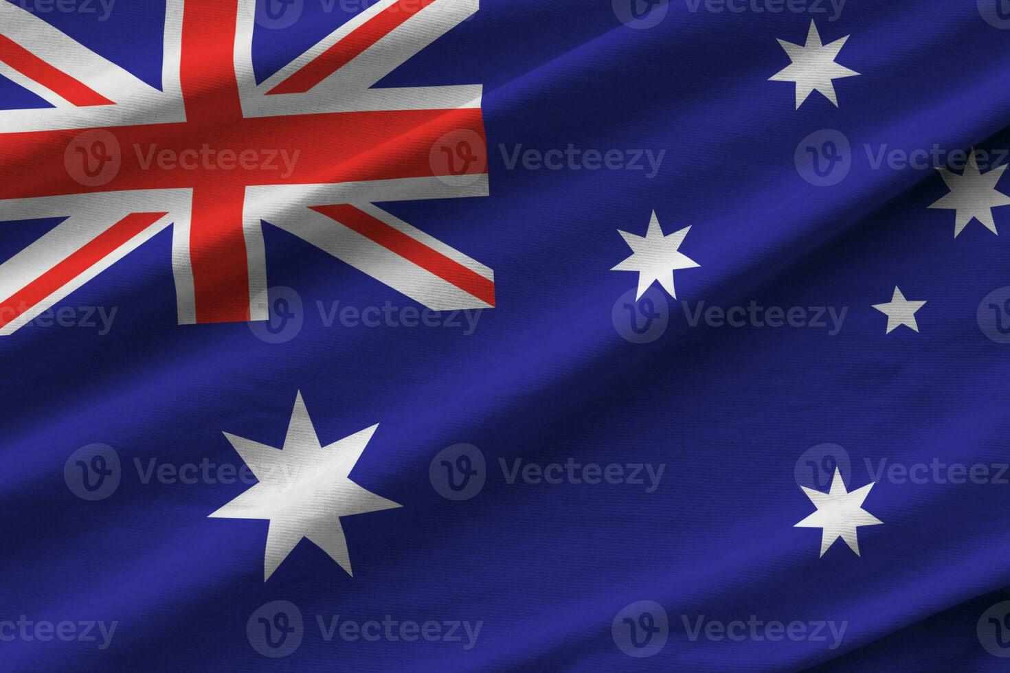 Australia flag with big folds waving close up under the studio light indoors. The official symbols and colors in banner photo