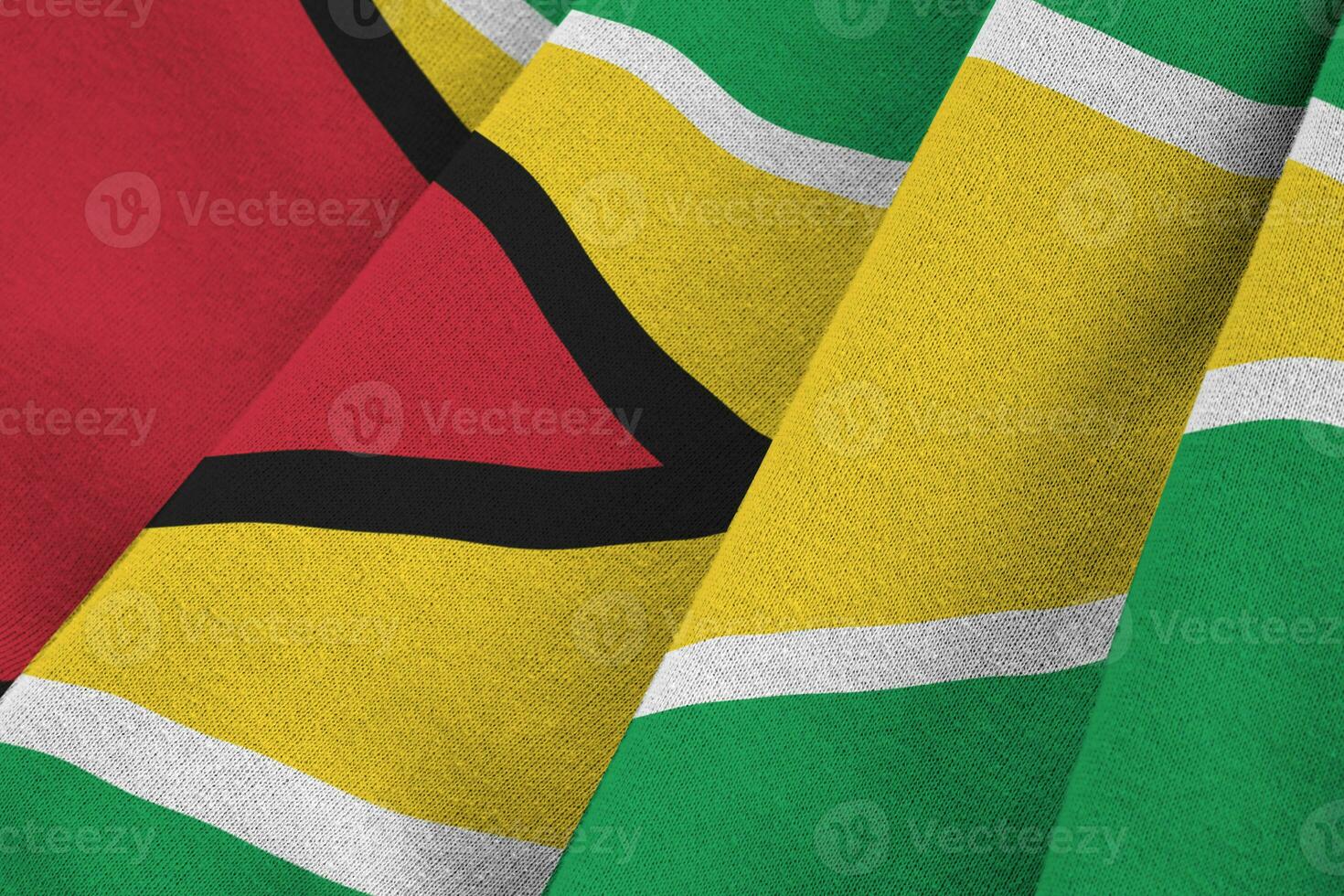 Guyana flag with big folds waving close up under the studio light indoors. The official symbols and colors in banner photo