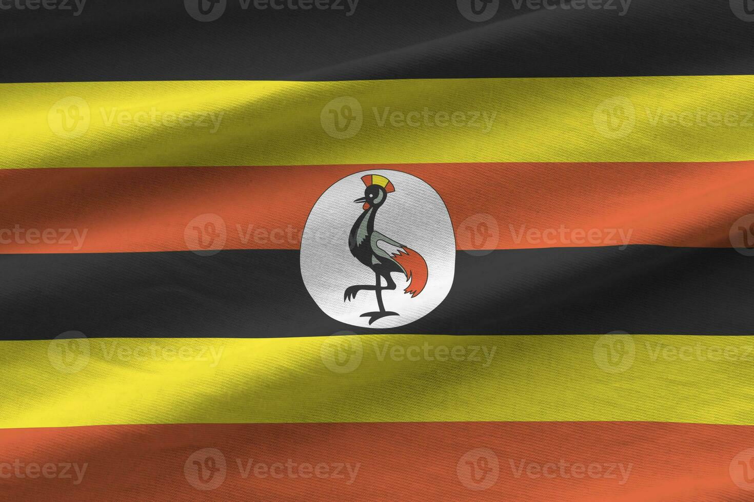 Uganda flag with big folds waving close up under the studio light indoors. The official symbols and colors in banner photo