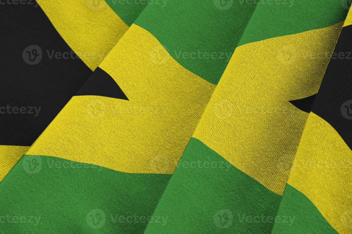 Jamaica flag with big folds waving close up under the studio light indoors. The official symbols and colors in banner photo