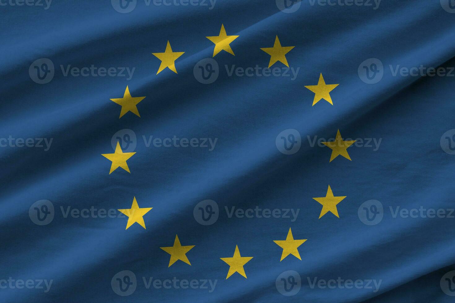 European union flag with big folds waving close up under the studio light indoors. The official symbols and colors in banner photo