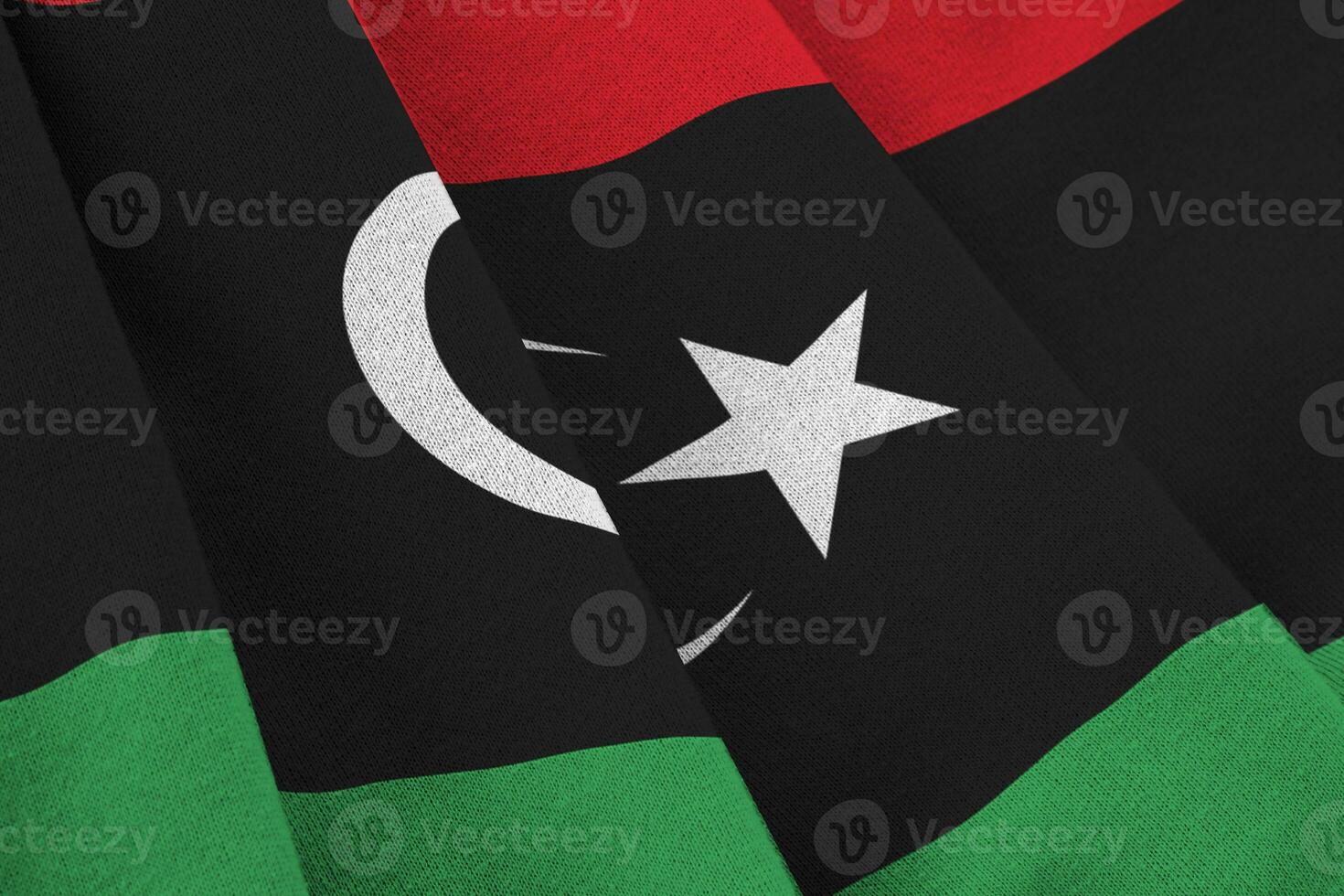 Libya flag with big folds waving close up under the studio light indoors. The official symbols and colors in banner photo