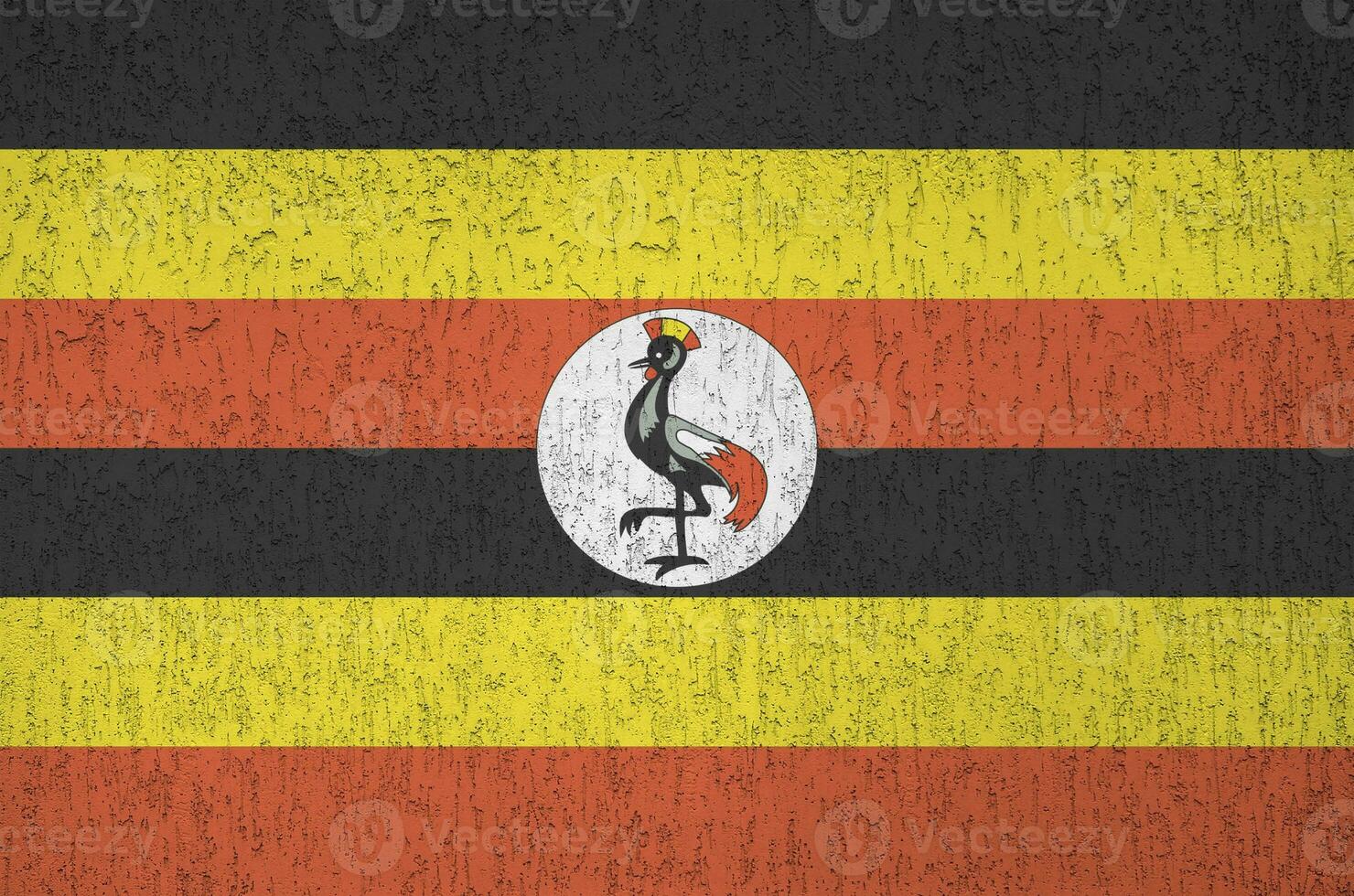 Uganda flag depicted in bright paint colors on old relief plastering wall. Textured banner on rough background photo