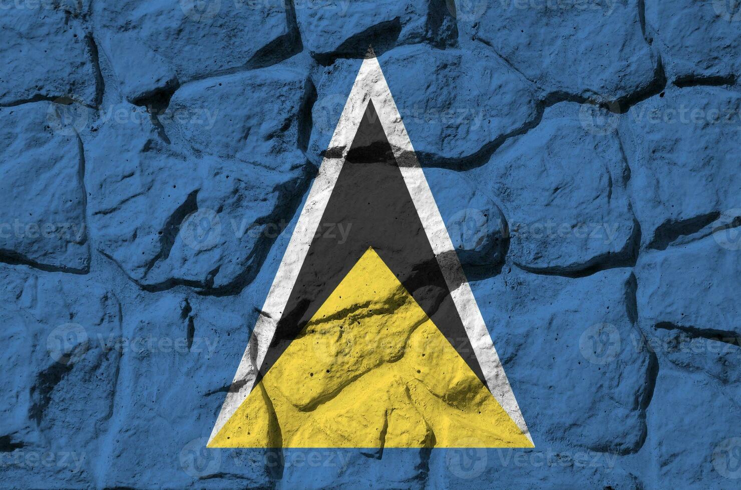 Saint Lucia flag depicted in paint colors on old stone wall closeup. Textured banner on rock wall background photo