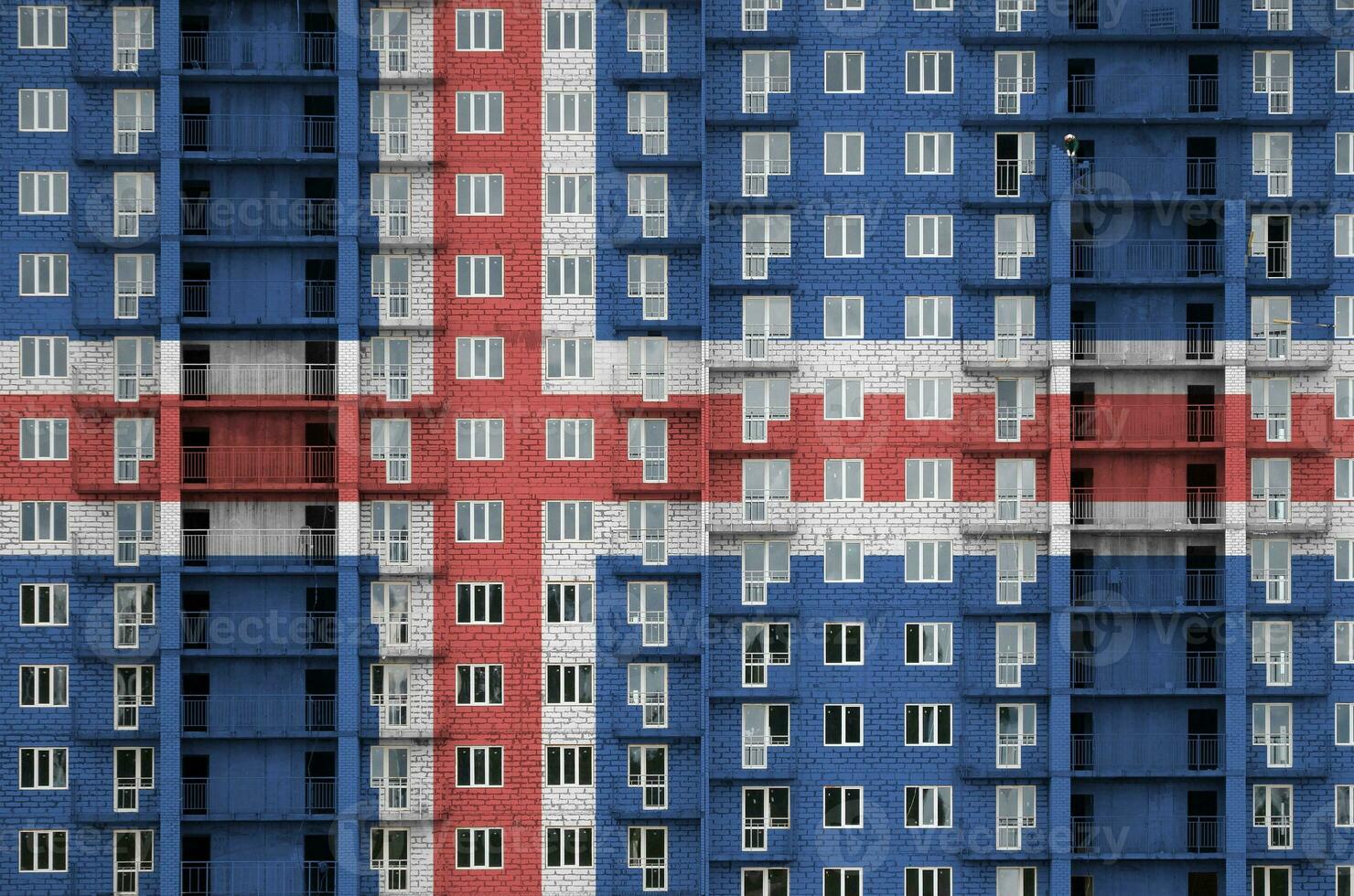 Iceland flag depicted in paint colors on multi-storey residental building under construction. Textured banner on brick wall background photo