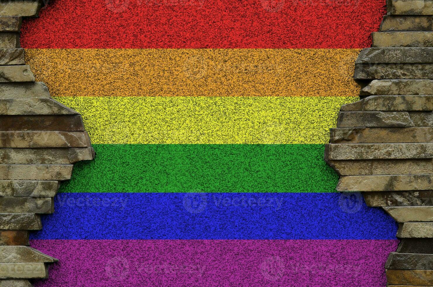 LGBT community flag depicted in paint colors on old stone wall closeup. Textured banner on rock wall background photo