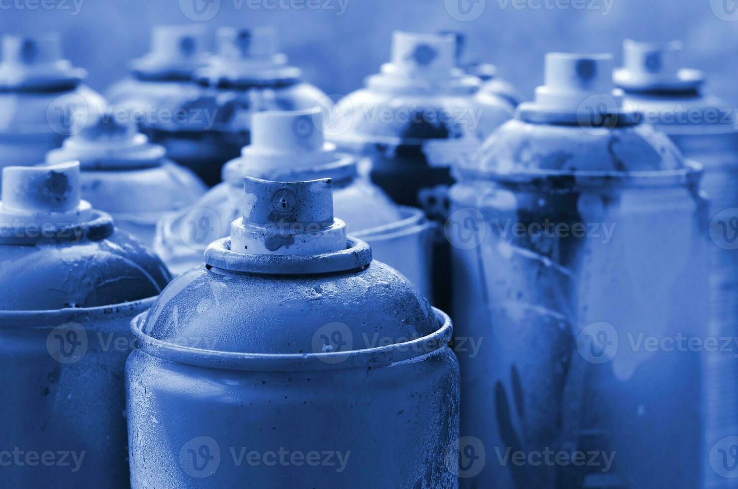 A lot of dirty and used aerosol cans of phantom classic blue colorpaint. Macro photograph with shallow depth of field. Selective focus on the spray nozzle photo