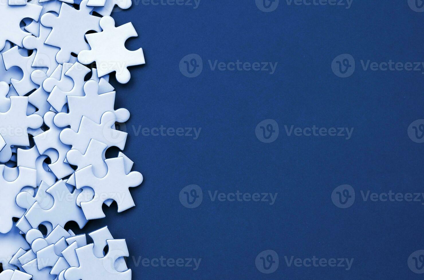 A pile of uncombed elements of a white jigsaw puzzle lies on the background of phantom classic blue color surface. Texture photo with copy space for text