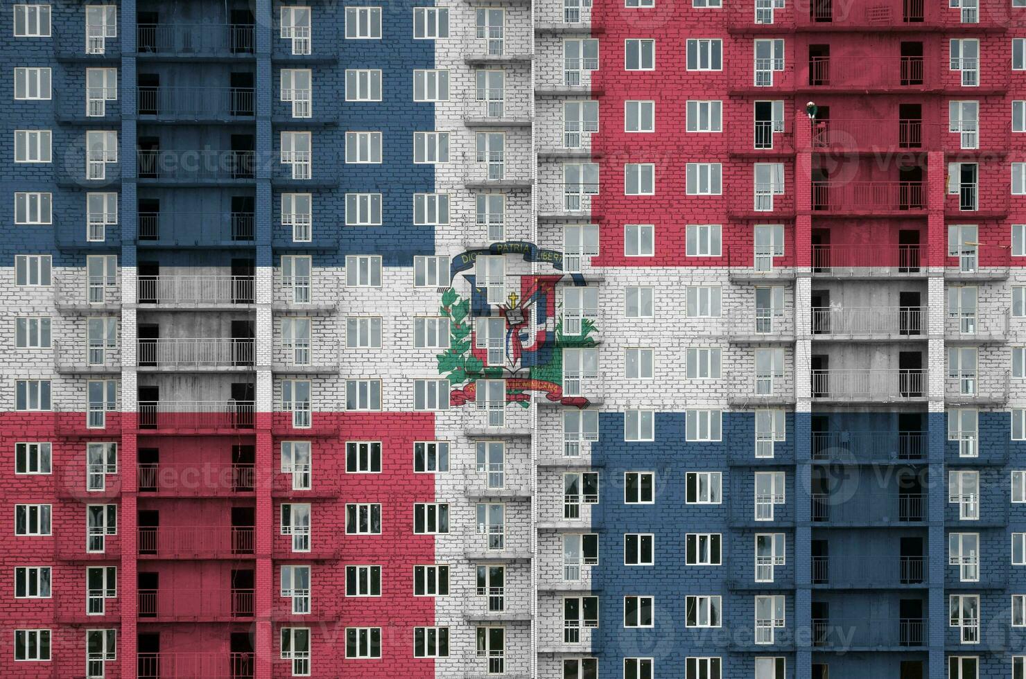 Dominican Republic flag depicted in paint colors on multi-storey residental building under construction. Textured banner on brick wall background photo
