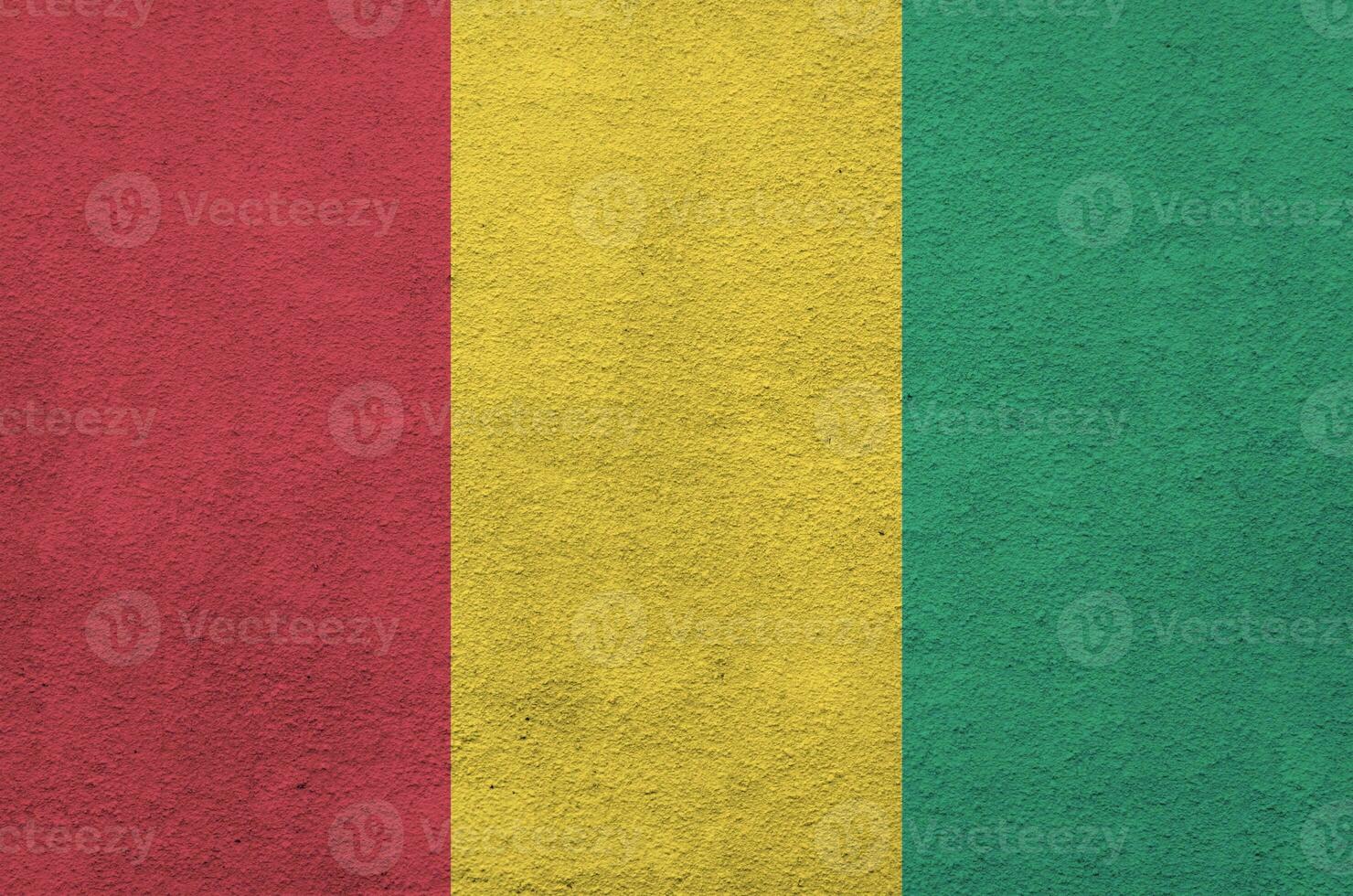 Guinea flag depicted in bright paint colors on old relief plastering wall. Textured banner on rough background photo