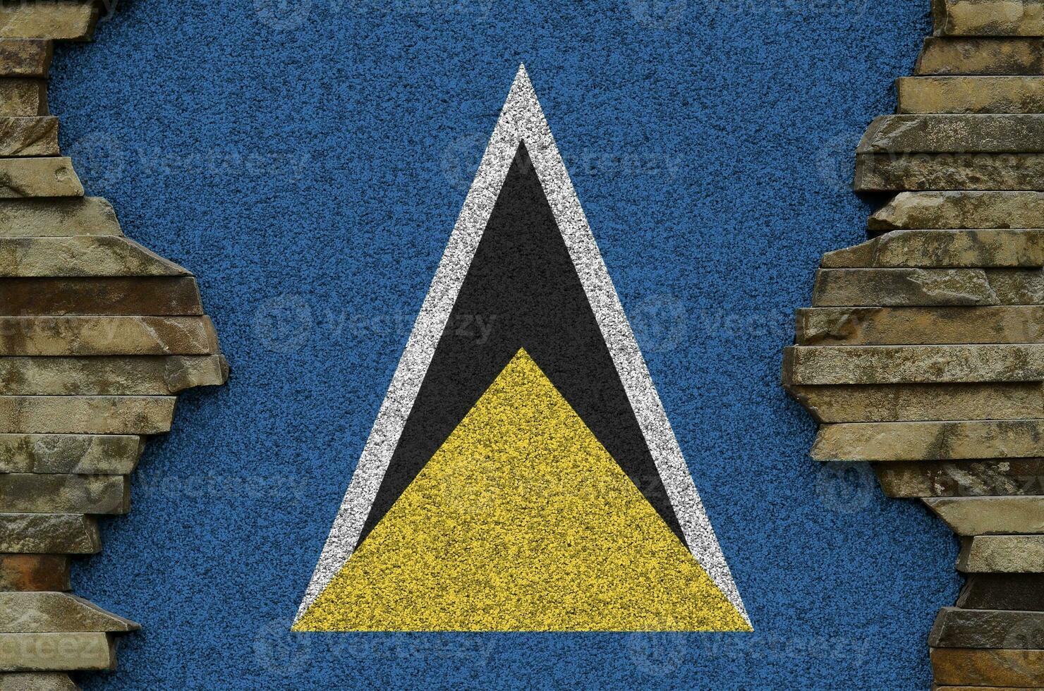 Saint Lucia flag depicted in paint colors on old stone wall closeup. Textured banner on rock wall background photo