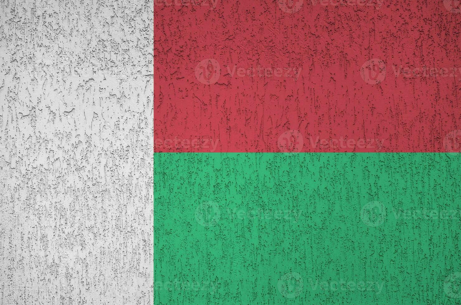 Madagascar flag depicted in bright paint colors on old relief plastering wall. Textured banner on rough background photo