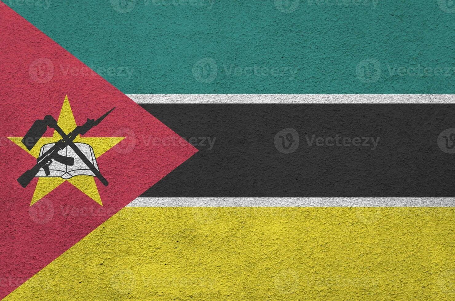 Mozambique flag depicted in bright paint colors on old relief plastering wall. Textured banner on rough background photo