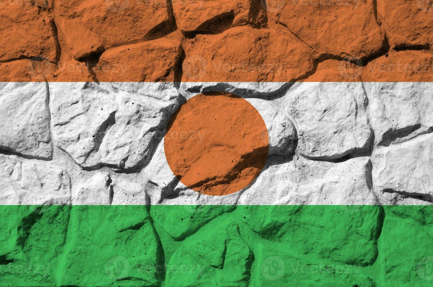 Niger flag depicted in paint colors on old stone wall closeup. Textured banner on rock wall background photo