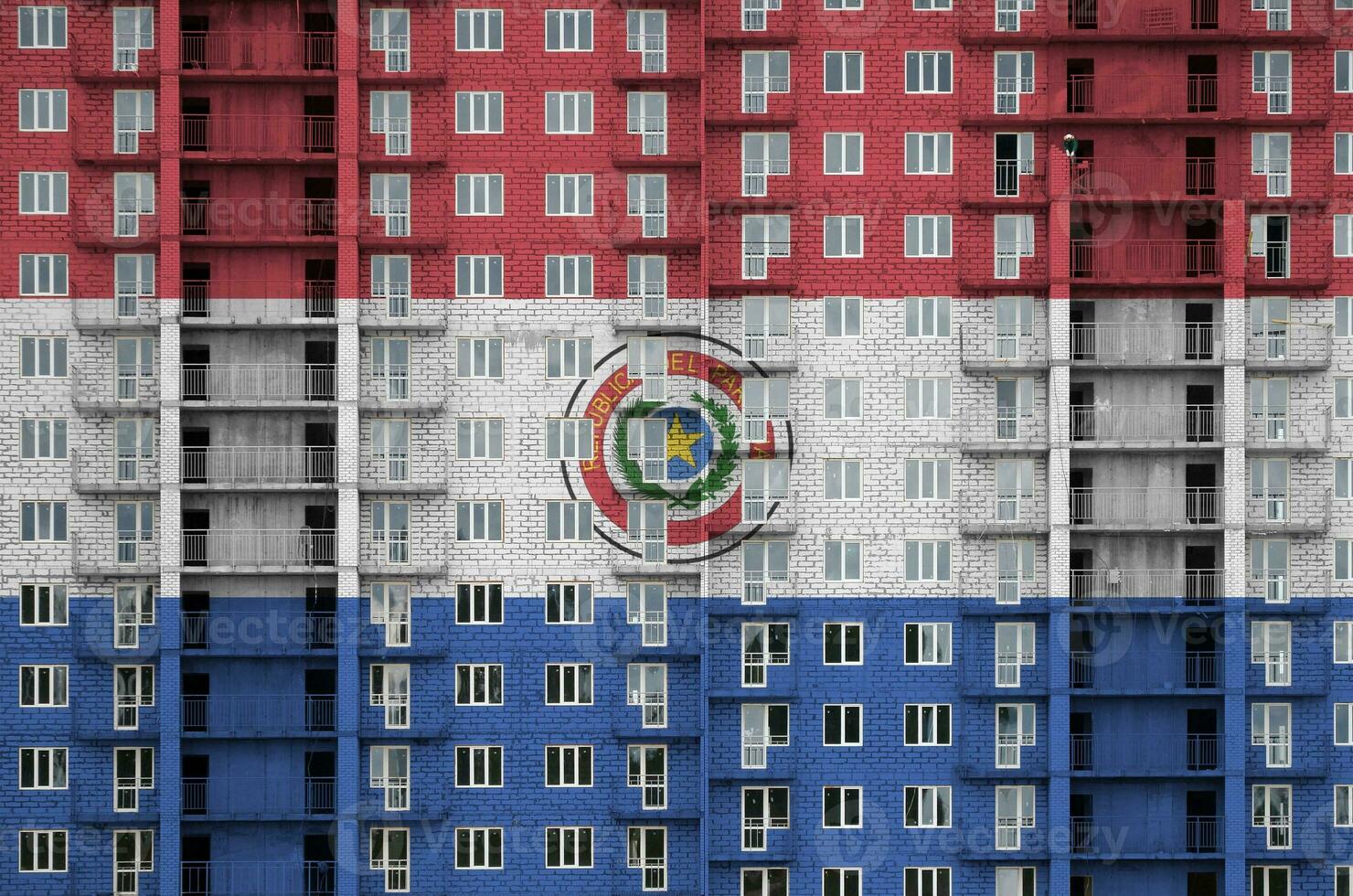 Paraguay flag depicted in paint colors on multi-storey residental building under construction. Textured banner on brick wall background photo