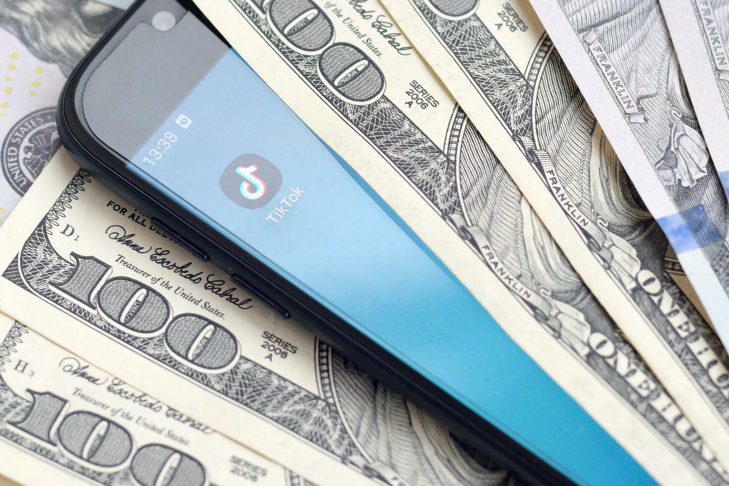 Smartphone screen with Tiktok app and lot of hundred dollar bills. Business and social networking concept photo