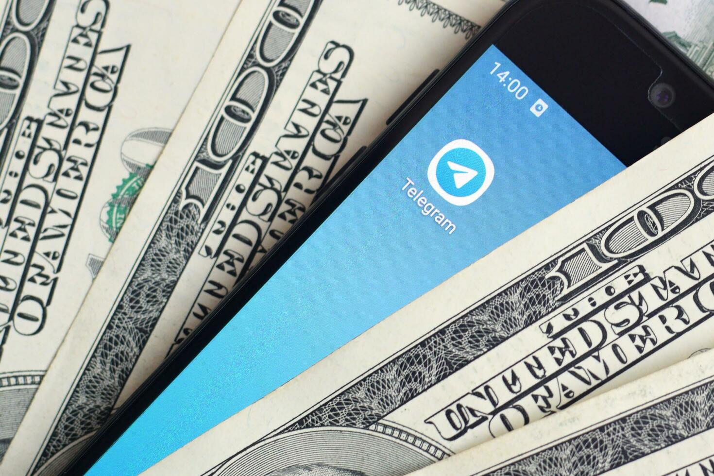 Smartphone screen with Telegram app and lot of hundred dollar bills. Business and social networking concept photo