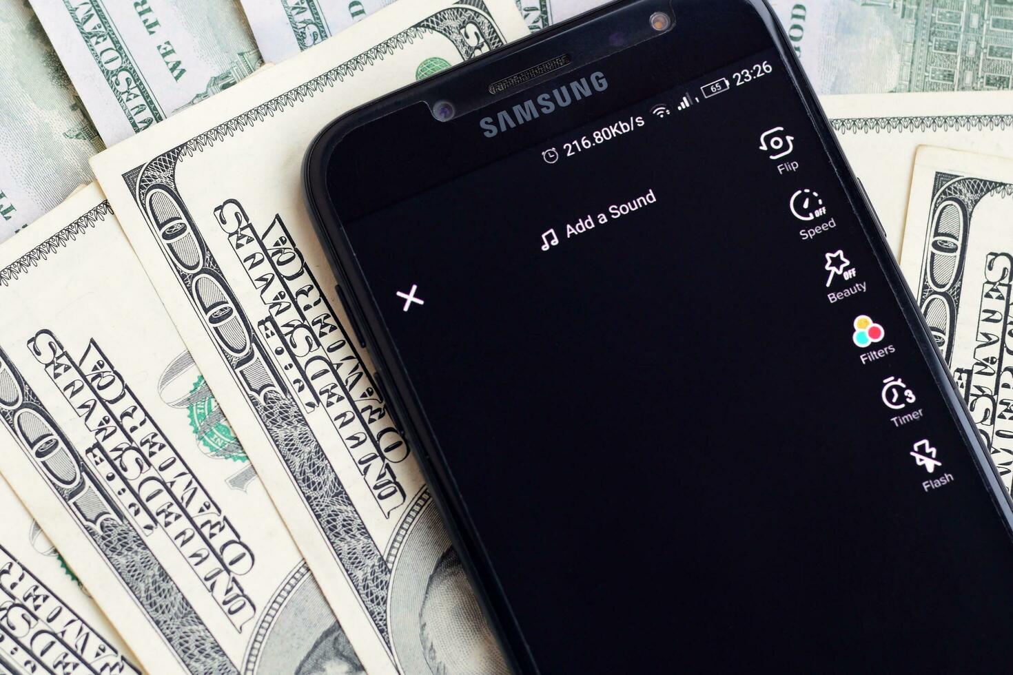 Smartphone screen with Tiktok app and lot of hundred dollar bills. Business and social networking concept photo