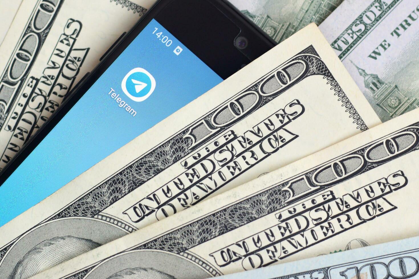 Smartphone screen with Telegram app and lot of hundred dollar bills. Business and social networking concept photo
