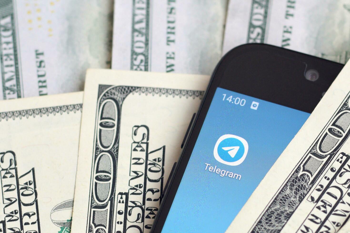 Smartphone screen with Telegram app and lot of hundred dollar bills. Business and social networking concept photo