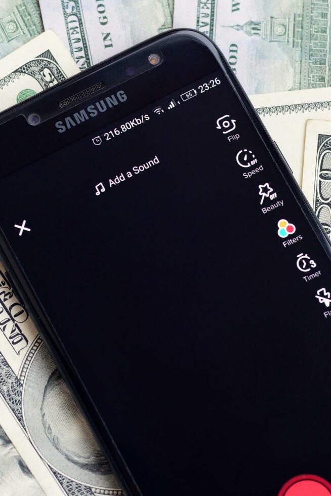 Smartphone screen with Tiktok app and lot of hundred dollar bills. Business and social networking concept photo