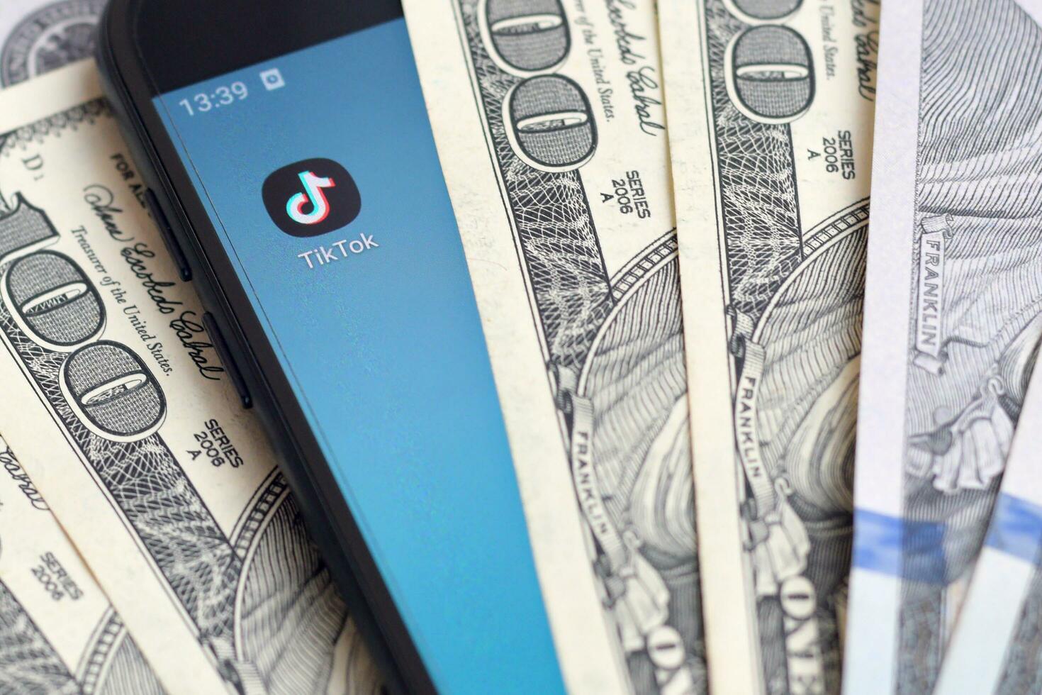 Smartphone screen with Tiktok app and lot of hundred dollar bills. Business and social networking concept photo