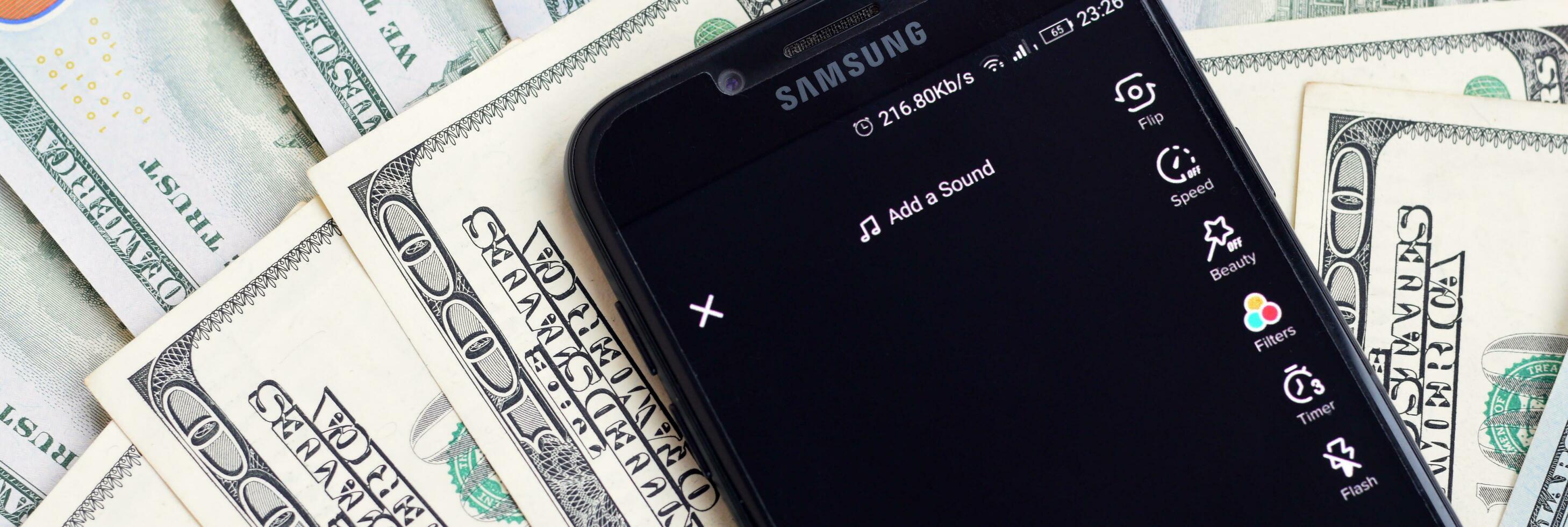 Smartphone screen with Tiktok app and lot of hundred dollar bills. Business and social networking concept photo