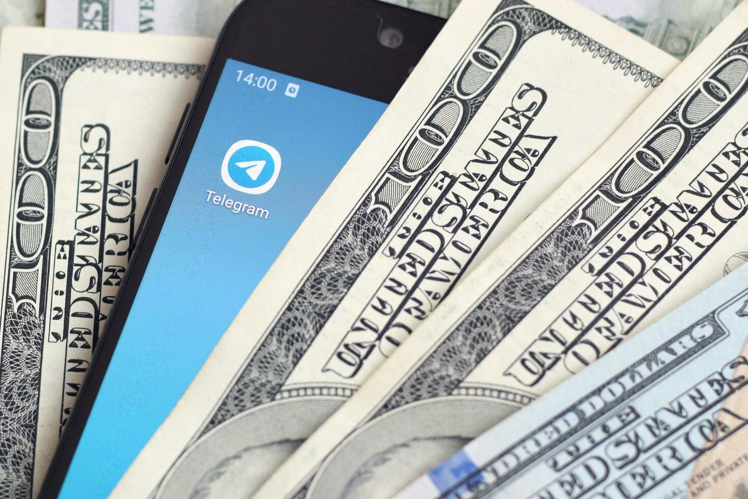 Smartphone screen with Telegram app and lot of hundred dollar bills. Business and social networking concept photo