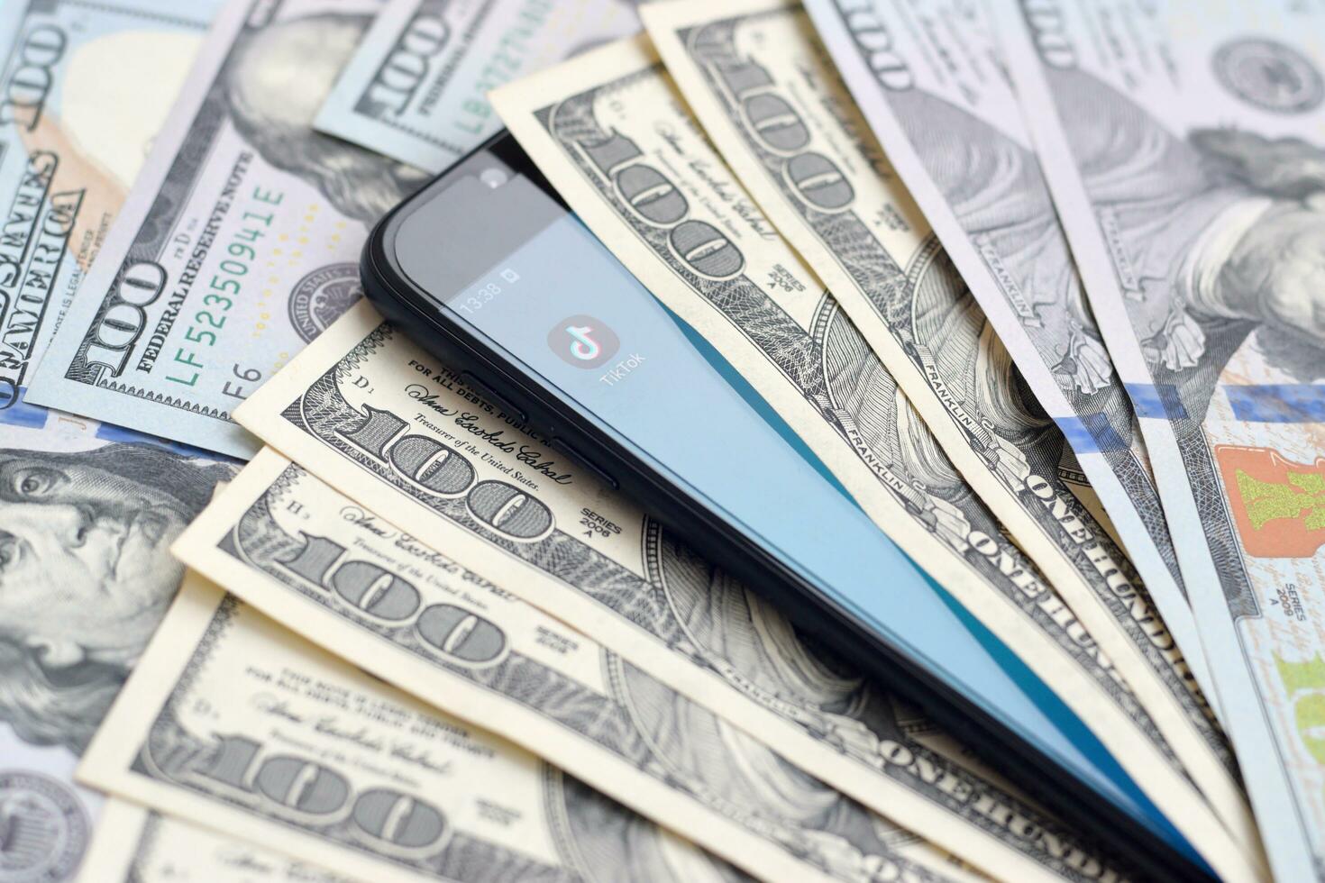 Smartphone screen with Tiktok app and lot of hundred dollar bills. Business and social networking concept photo