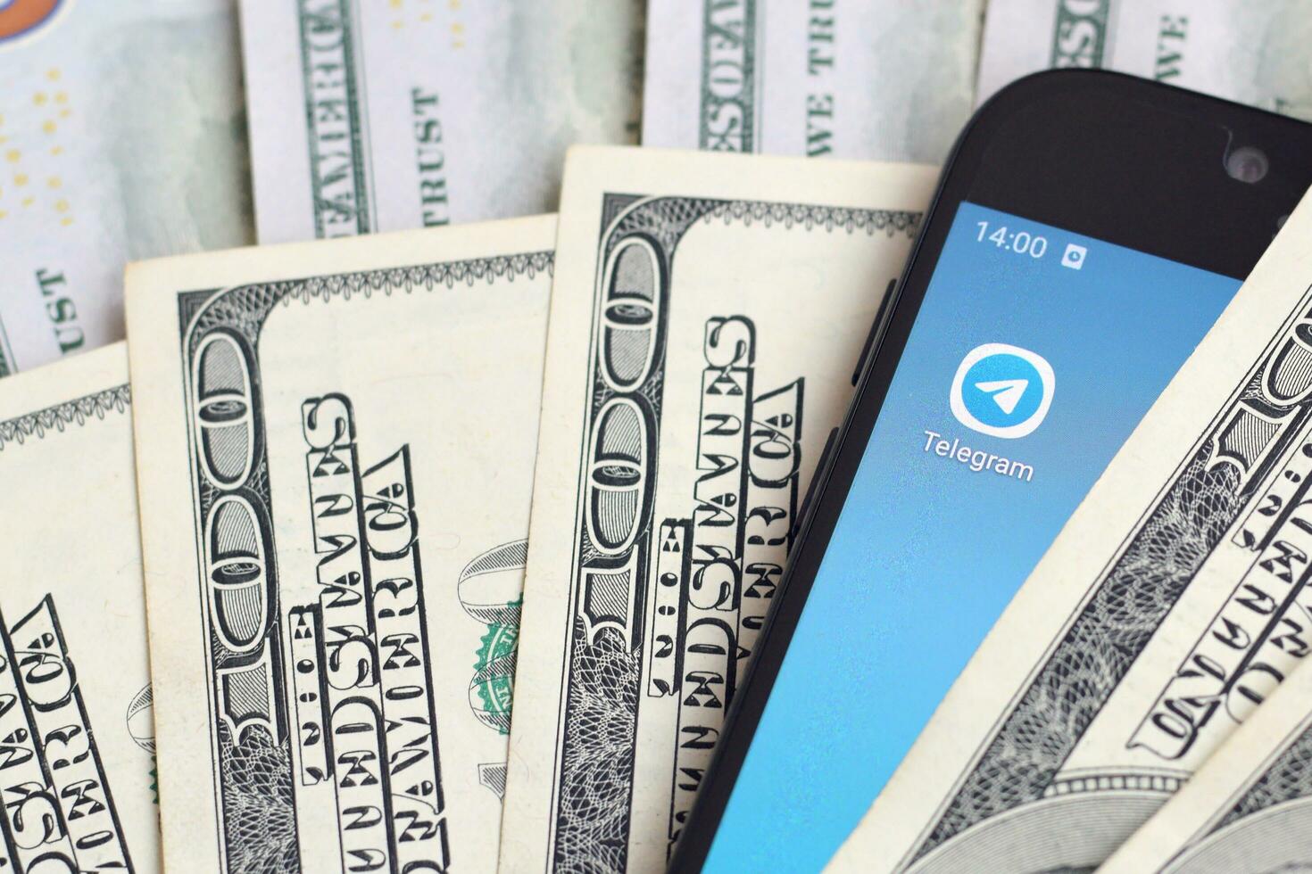 Smartphone screen with Telegram app and lot of hundred dollar bills. Business and social networking concept photo