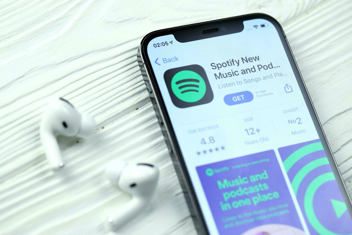 KHARKOV, UKRAINE - MARCH 5, 2021 Spotify icon and application from App store on iPhone 12 pro display screen with airpods pro on white table photo