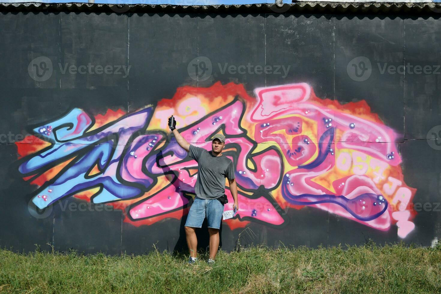 Young caucasian male graffiti artist drawing big street art painting in blue and pink tones photo