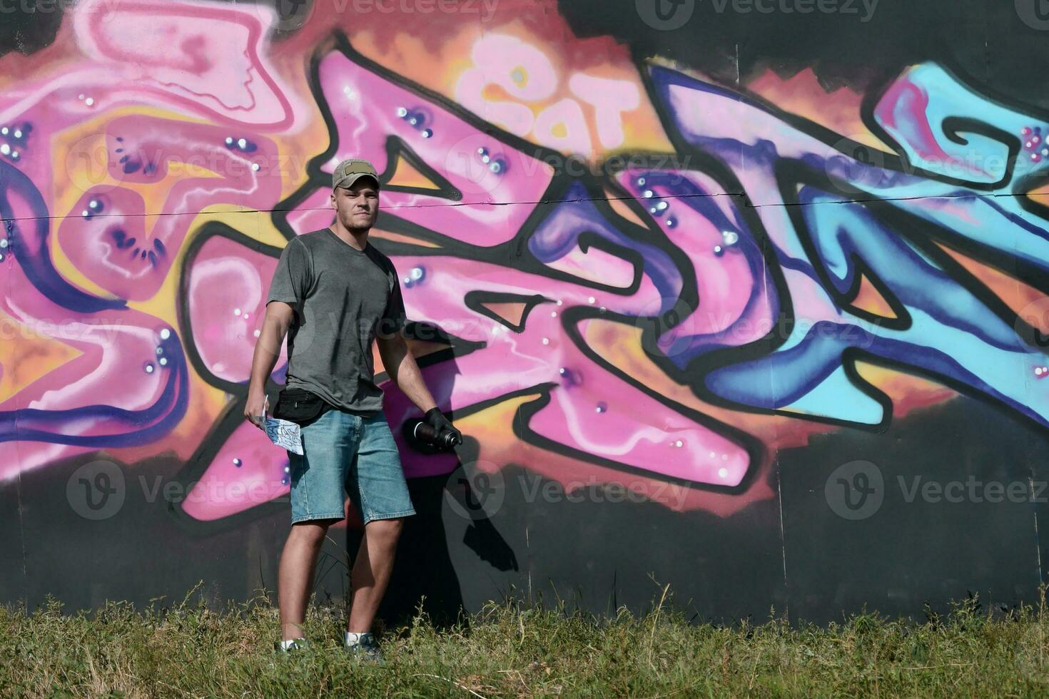 Young caucasian male graffiti artist drawing big street art painting in blue and pink tones photo