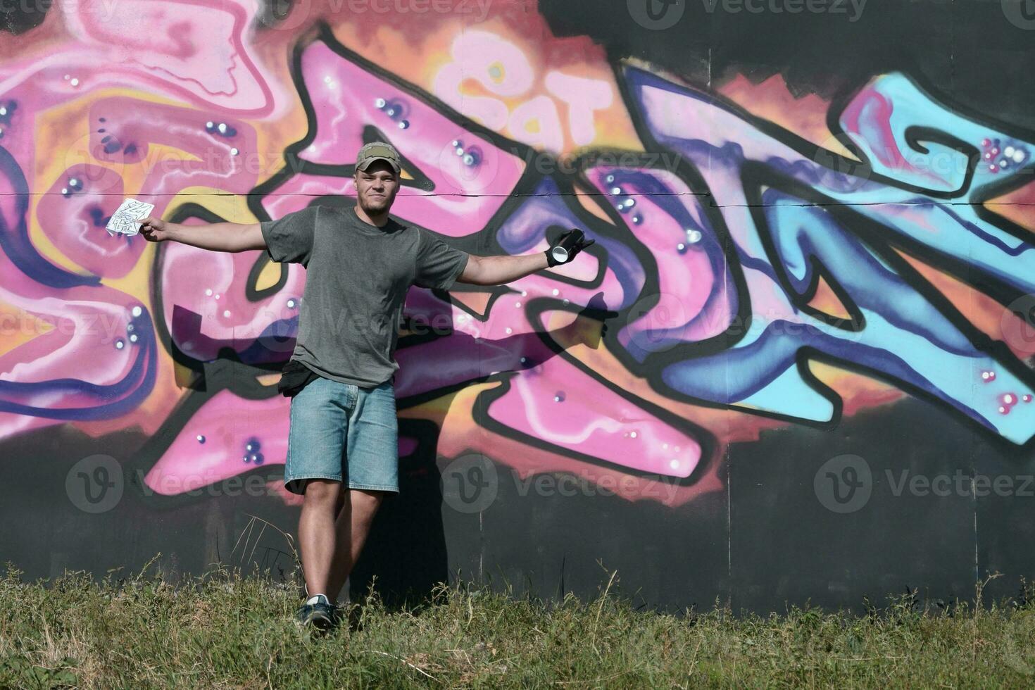 Young caucasian male graffiti artist drawing big street art painting in blue and pink tones photo