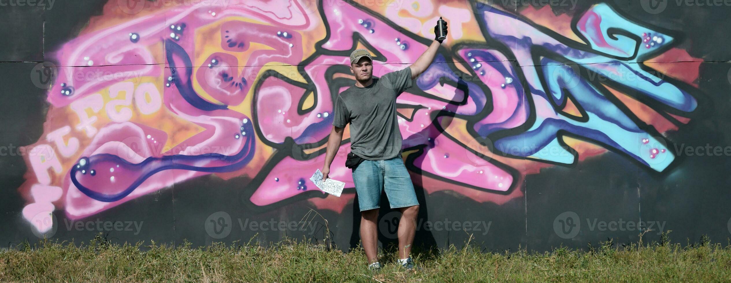 Young caucasian male graffiti artist drawing big street art painting in blue and pink tones photo