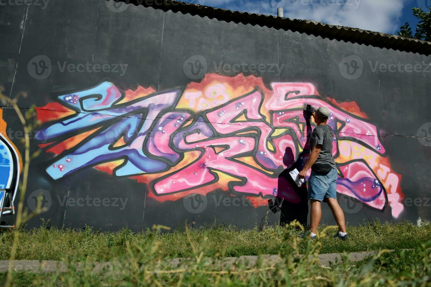 Young caucasian male graffiti artist drawing big street art painting in blue and pink tones photo
