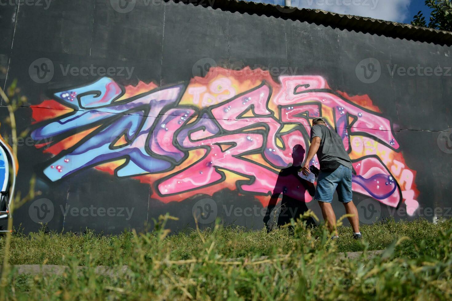 Young caucasian male graffiti artist drawing big street art painting in blue and pink tones photo