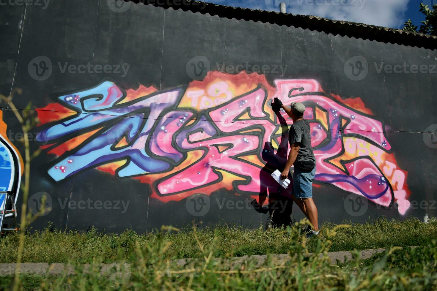 Young caucasian male graffiti artist drawing big street art painting in blue and pink tones photo