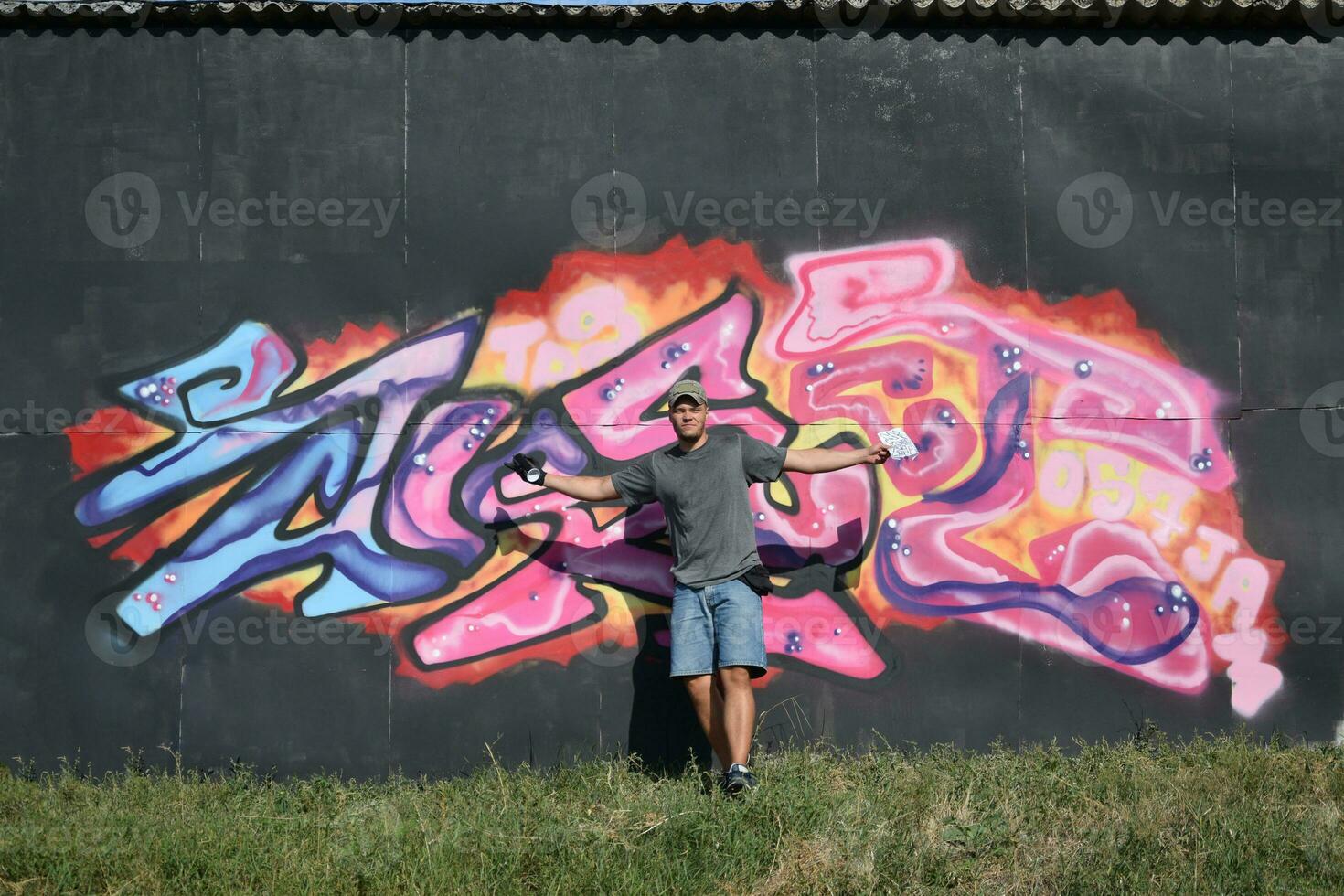Young caucasian male graffiti artist drawing big street art painting in blue and pink tones photo
