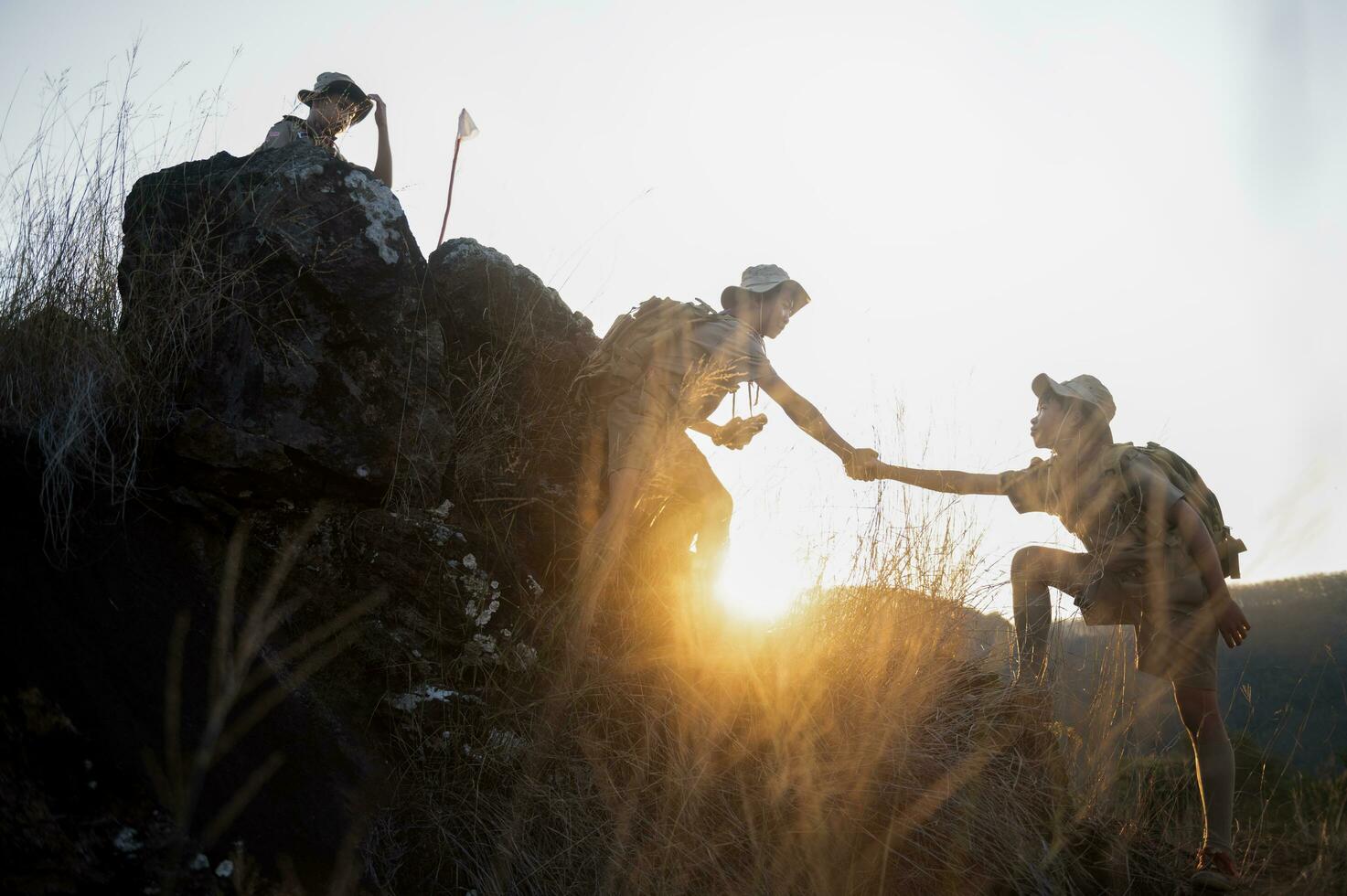 Boy Scouts team climbing with backpacks standing on mountain Boy Scouts rejoice at rock climbing success in Scout camp at sunset. Scout camp view. photo