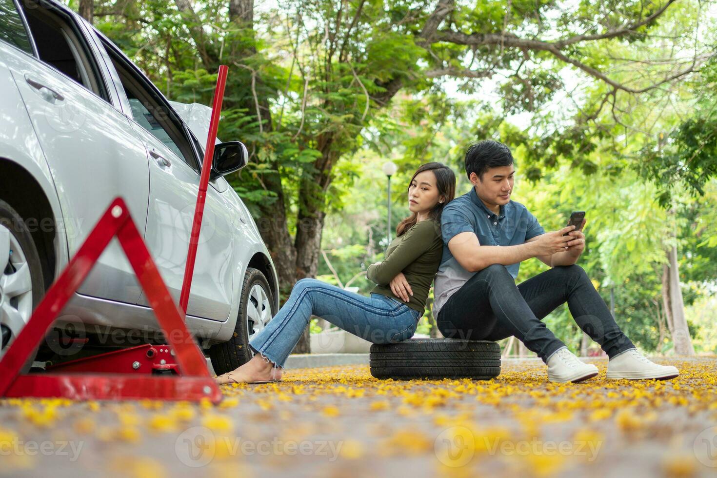 Asian couple using smartphone for assistance after a car breakdown on street. Concept of vehicle engine problem or accident and emergency help from Professional mechanic photo