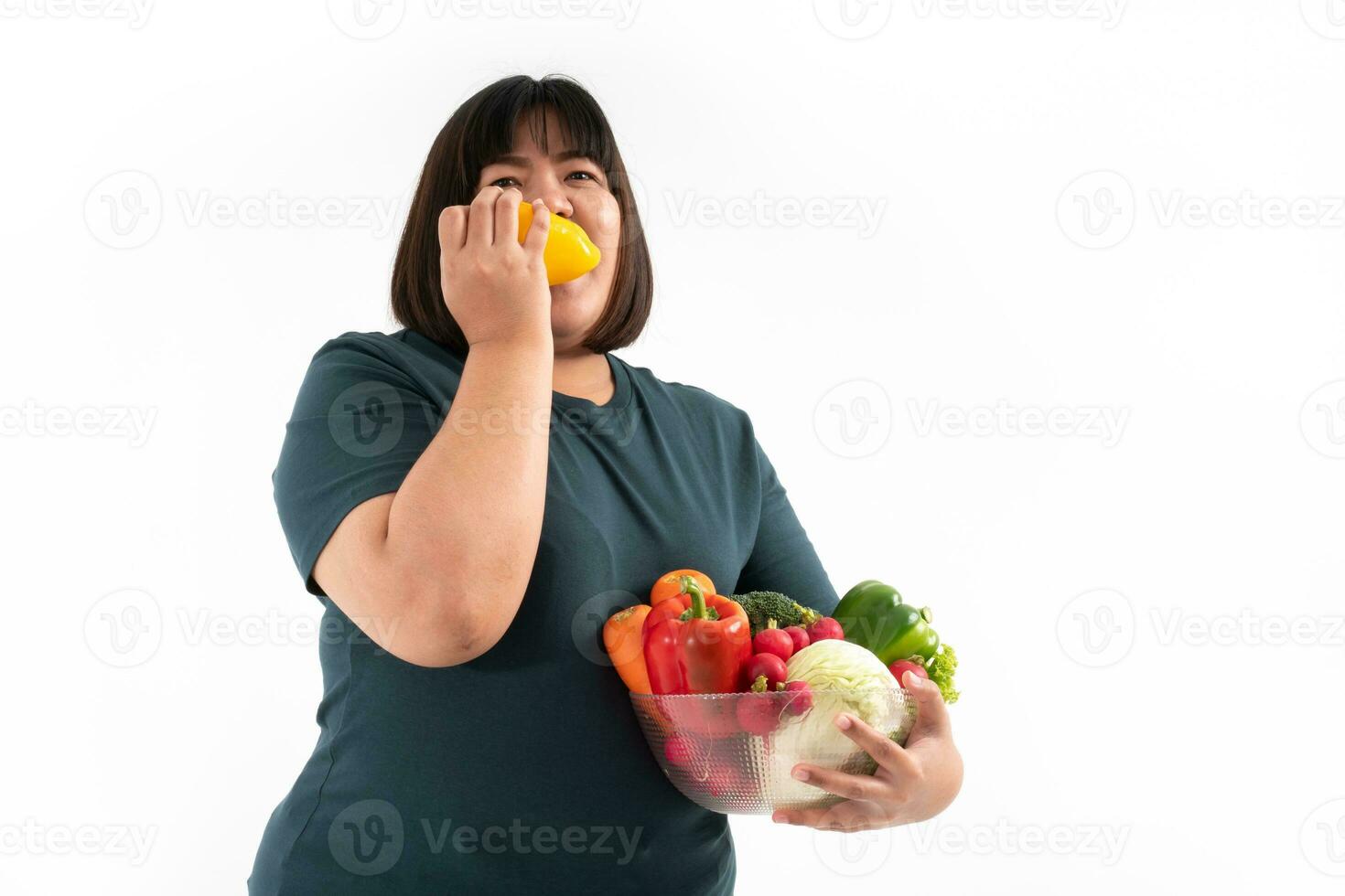 Happy Asian overweight woman Eating,  holding a vegetable basket, and smiling on isolated white background, Concept of good health comes from eating a nutritious diet. photo