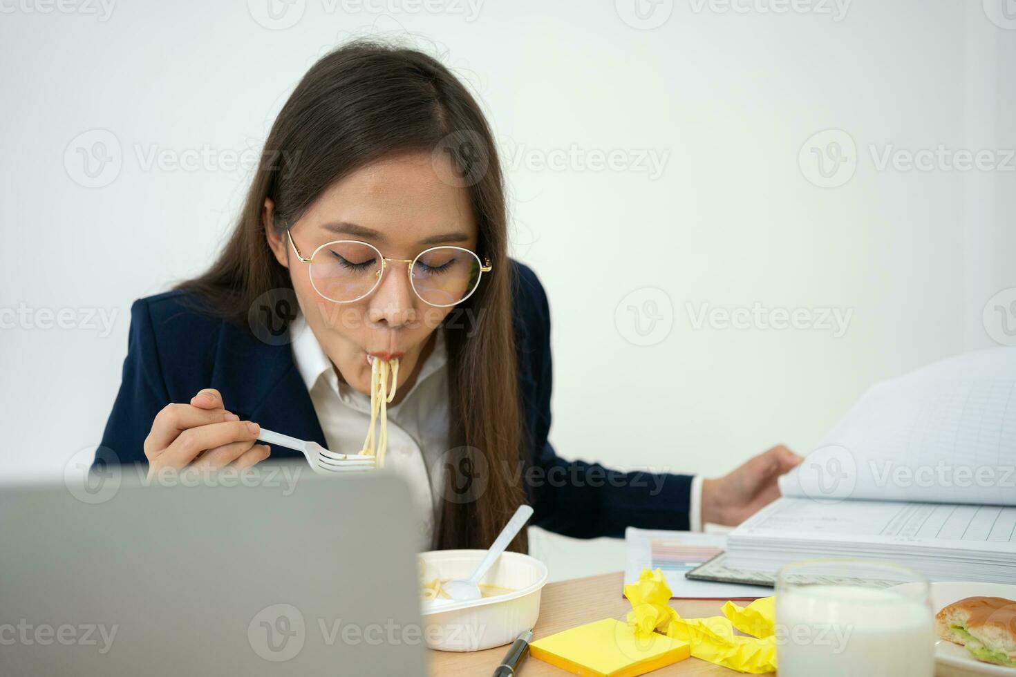 Busy and tired businesswoman eating spaghetti for lunch at the Desk office and working to deliver financial statements to a boss. Overworked and unhealthy for ready meals, burnout concept. photo
