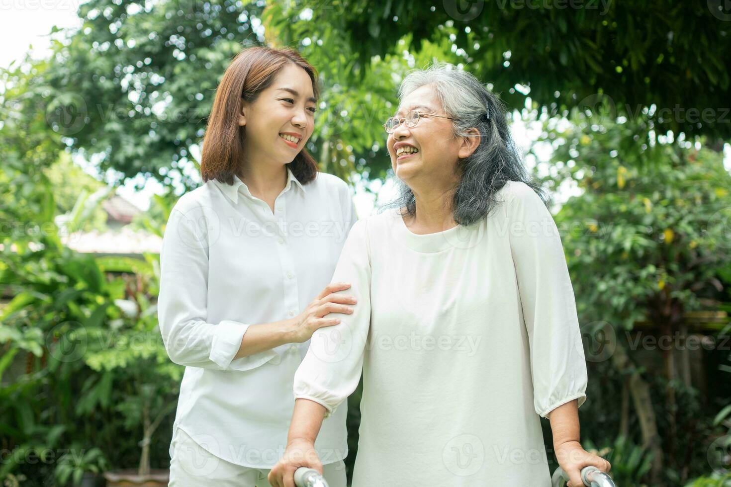 An old elderly Asian woman uses a walker and walking in the backyard with her daughter.  Concept of happy retirement With care from a caregiver and Savings and senior health insurance photo