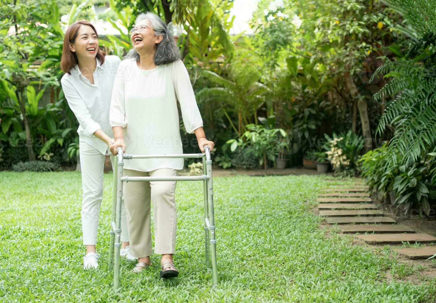 An old elderly Asian woman uses a walker and walking in the backyard with her daughter.  Concept of happy retirement With care from a caregiver and Savings and senior health insurance photo