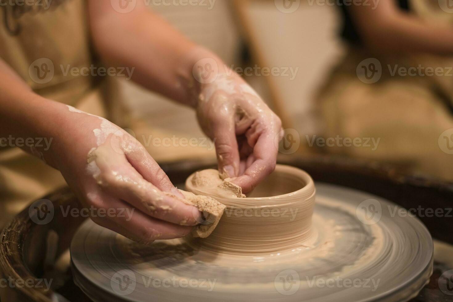 Potter girl works on potter's wheel, making ceramic pot out of clay in pottery workshop photo