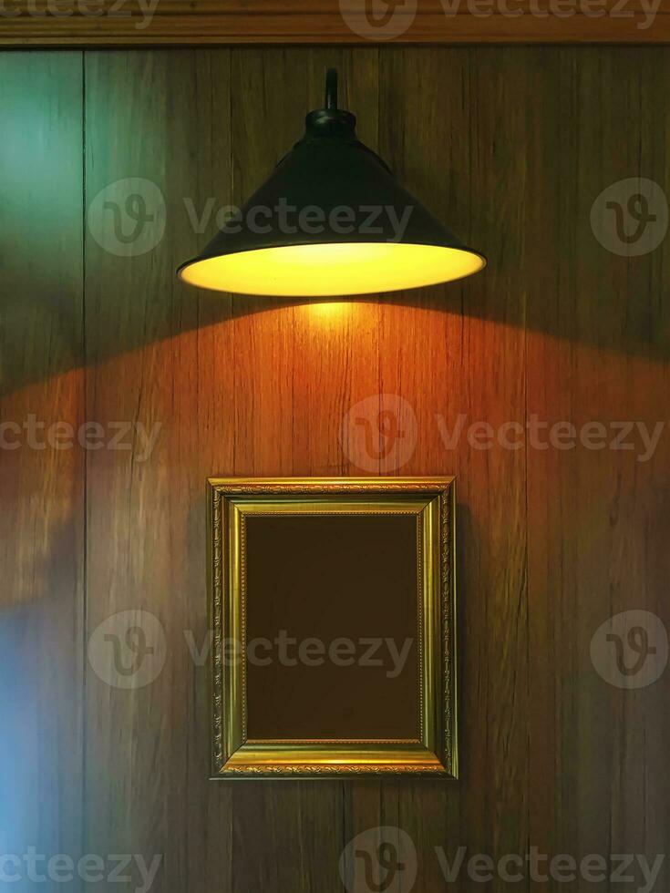 A wooden wall with picture frames under a yellow lamp. photo