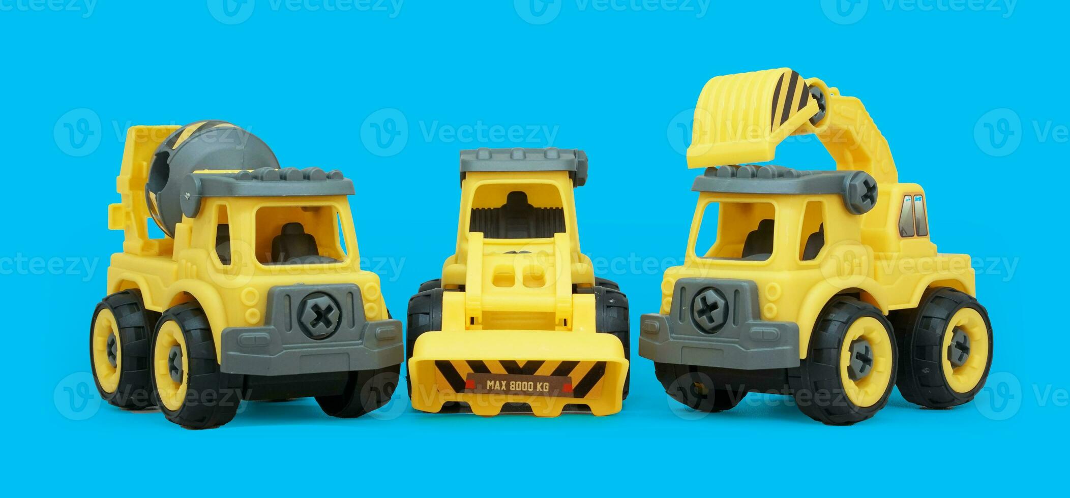 yellow plastic toy of concrete mixer and ecavator truck isolated on blue background. heavy construction vehicle on low angle shoot. photo